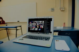 A computer sits on a desk with a virtual meeting in progress
