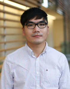 Image of a man with black hair wearing glasses and a button-down shirt